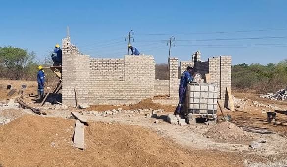 Builders raising brick walls on a new site with a water tank beside them