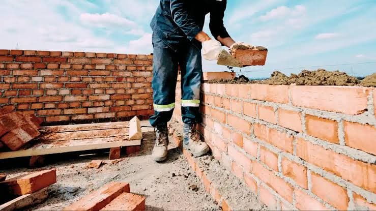 A builder placing a brick on a wall under construction