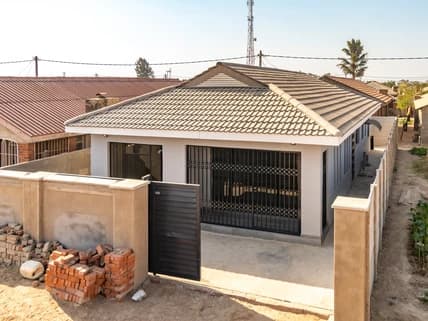 A completed house with a tiled roof behind a plastered boundary wall and steel gate