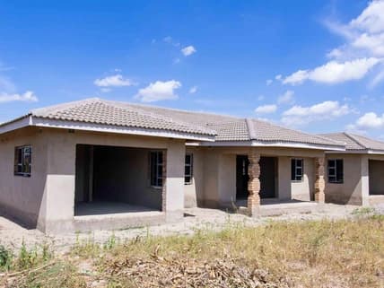 A plastered house shell under a new tiled roof, with verandah pillars, before finishing