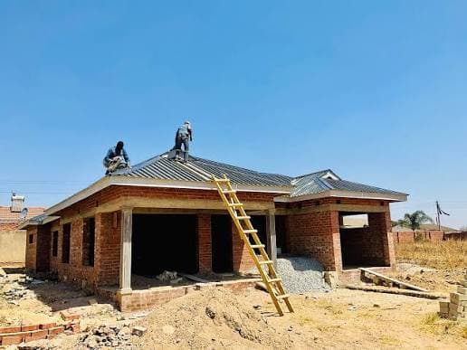 Roofers fixing sheeting on a brick house, with a ladder against the wall